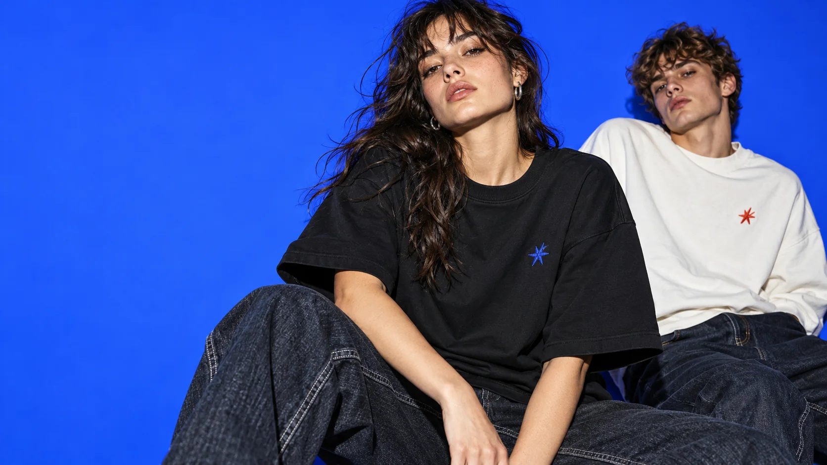 Originalt kampagnekoncept: voksne modeller i streetwear med små broderidetaljer på blå baggrund